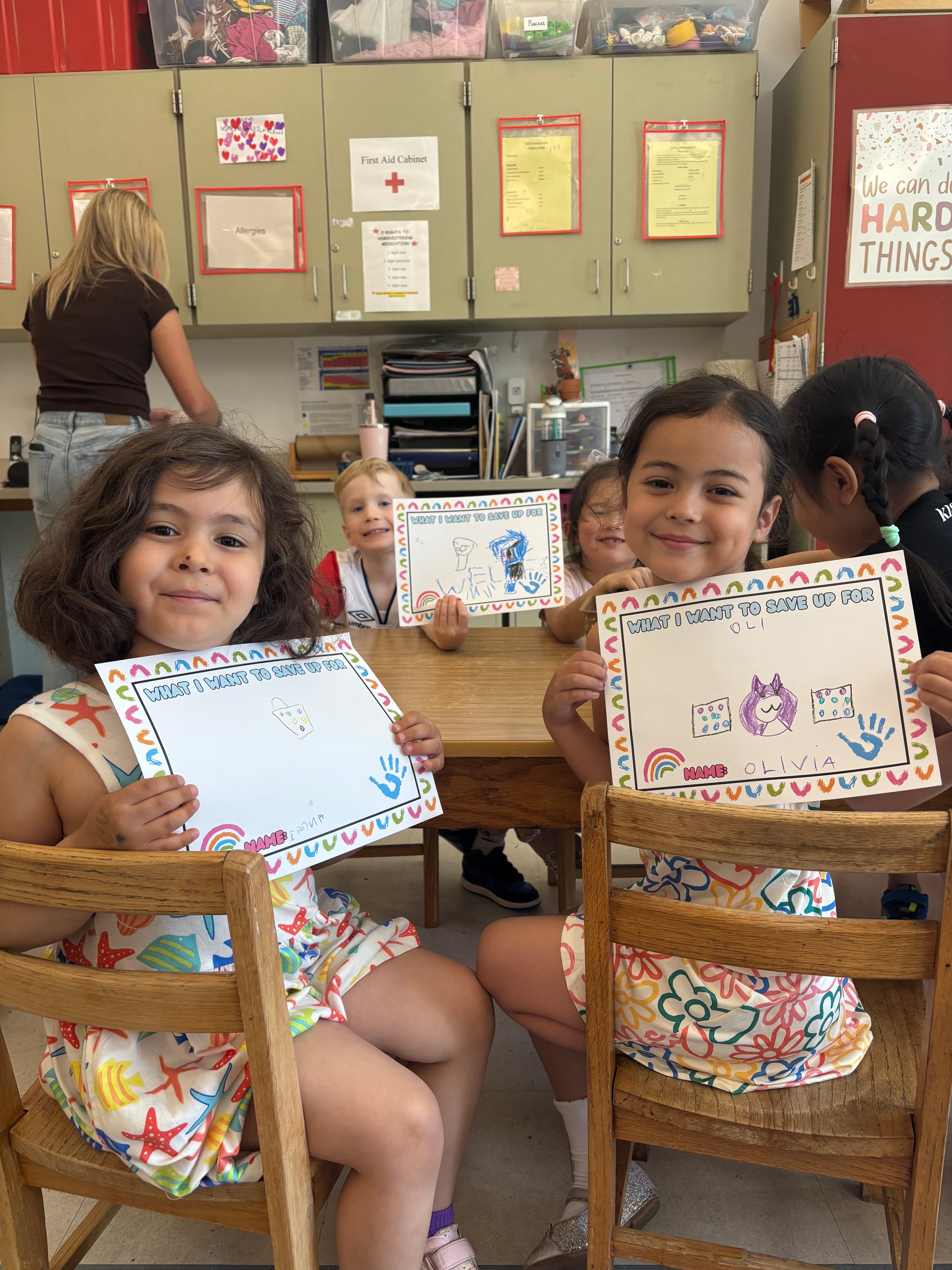 Two preschoolers proudly holding up their “What I want to save up for” drawings.