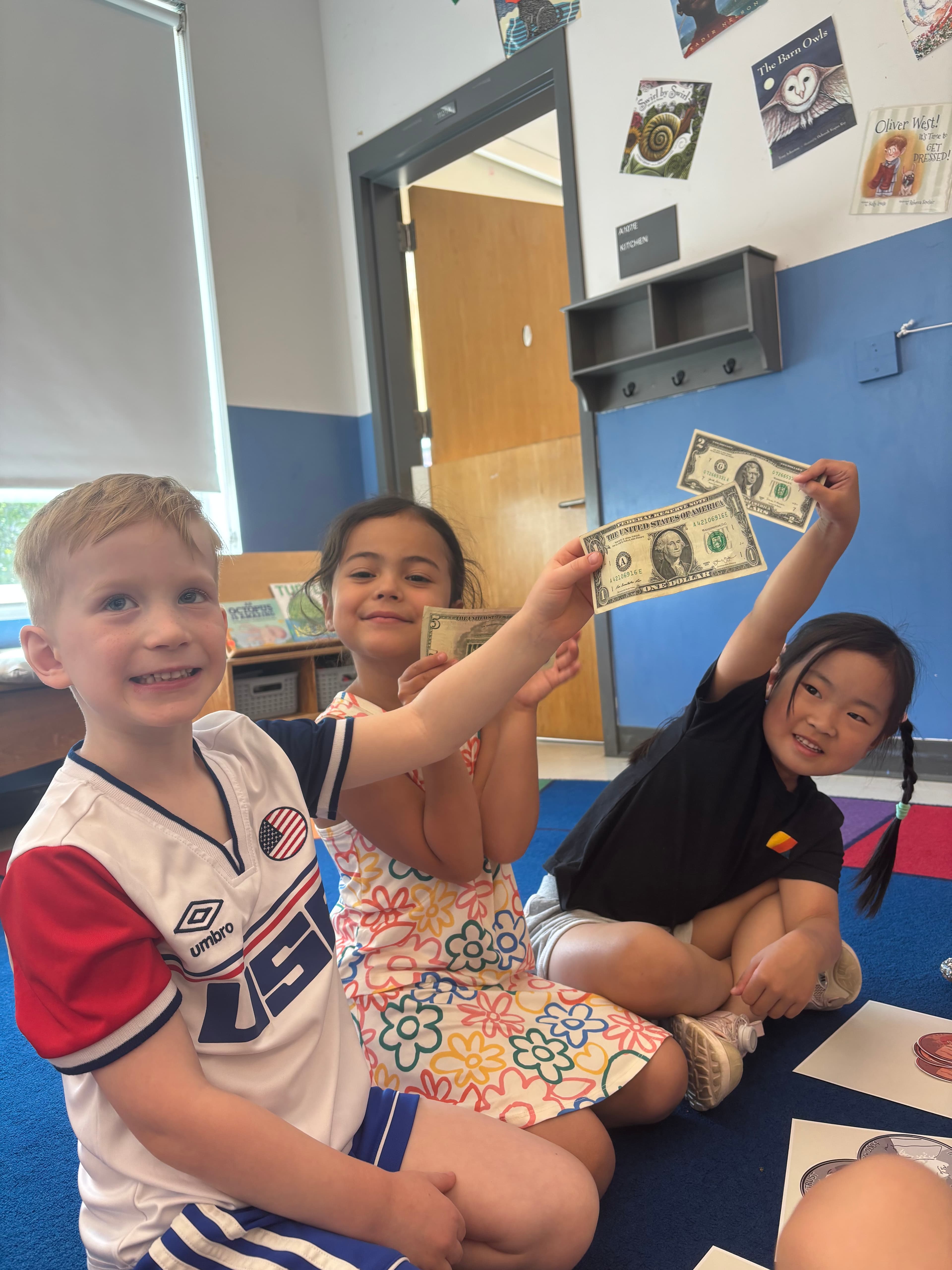 Three preschoolers smiling and holding up dollar bills during the lesson.
